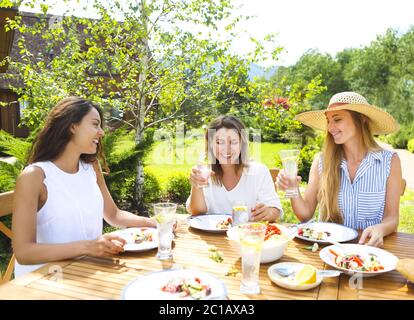 Glückliche Freundinnen mit Gläsern Limonade am Esstisch Stockfoto