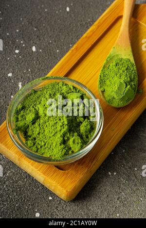 Selektiver Fokus, japanisches grünes Matcha-Teepulver auf einem Holztablett auf schwarzem Hintergrund Stockfoto