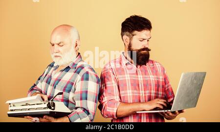 Mitbewerber: Vater und Sohn, Familiengeneration, Technologiekampf. Modernes Leben: Retro-Schreibmaschine im Vergleich zum Laptop. Neue Technologie. Jugend vs. Alter. Geschäftsansatz. Zwei bärtige Männer. Vintage-Schreibmaschine. Stockfoto