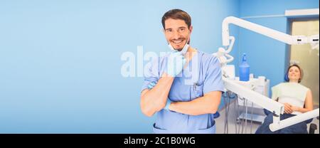 Junge lächelnd schöner männlicher Arzt in medizinischen Uniform, Einweg-medizinische Gesichtsmaske mit Geräten in der Zahnmedizin Büro und glücklichen Patienten in der Stockfoto