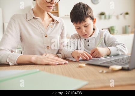 Cropped Porträt von jungen Mutter hilft Sohn online studieren, während am Schreibtisch sitzen und mit Laptop in gemütlichen Zuhause Interieur Stockfoto