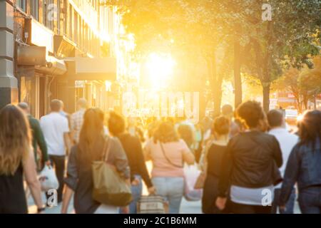 Eine Gruppe von Männern und Frauen, die die Straße entlang gehen, mit hellem Licht des Sonnenuntergangs im Hintergrund, New York City NYC Stockfoto