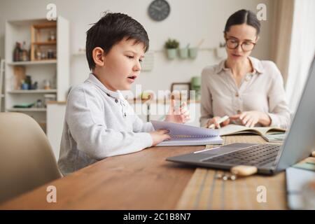 Warm-toned Seitenansicht Porträt von niedlichen Jungen schriftlich im Notebook, während zu Hause in gemütlichen Küche Interieur studieren Stockfoto