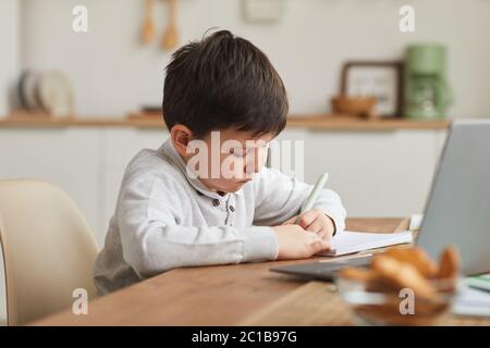 Warm-getönte Porträt von niedlichen Jungen schriftlich in Notebook, während zu Hause in gemütlichen Innenraum, Kopierer Raum zu studieren Stockfoto