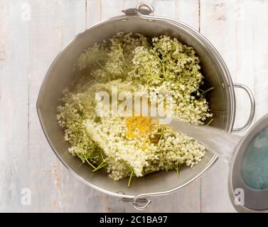 Gieße kochendes Wasser in eine Pfanne mit Holunderblüten und Zitronen- und Orangenschale, um es zu kochen. Stockfoto