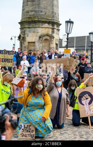 Richmond, North Yorkshire, Großbritannien - 14. Juni 2020: BLM-Demonstranten knien auf Kopfsteinpflaster im Richmond Marketplace und halten Schilder, während sie PSA-Gesichtsmasken tragen Stockfoto