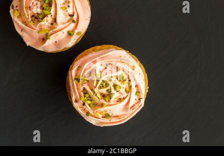 Zwei rosa Tasse Kuchen mit Pistazien Nuss Streuseln Nahaufnahme auf schwarzem Hintergrund - Draufsicht Foto Stockfoto