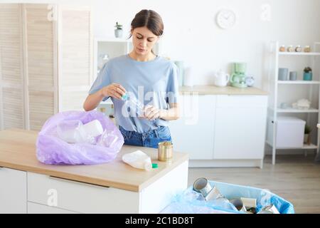 Junge Frau Recycling der Plastikflaschen, die sie in die Packung, während sie in der Küche stehen Stockfoto