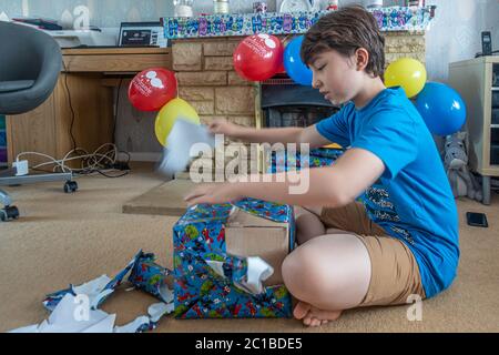 Ein Junge sitzt auf dem Boden und wickelt ein Geburtstagsgeschenk ab, das Geschenkpapier wird begeistert abgezerreißt. Stockfoto