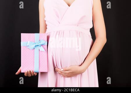 Cropped Bild von schwangeren Frau in rosa Kleid mit rosa gepunkteten Geschenkbox auf schwarzem Hintergrund. Warten auf ein Baby Mädchen. Speicherplatz kopieren. Stockfoto