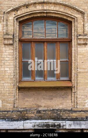 Vintage Bogenfenster in der Wand aus gelben Ziegel. Schwarzes Glas in einem kastanienbraunen dunkelroten Holzrahmen. Das Konzept des antiken Jahrgangs Stockfoto