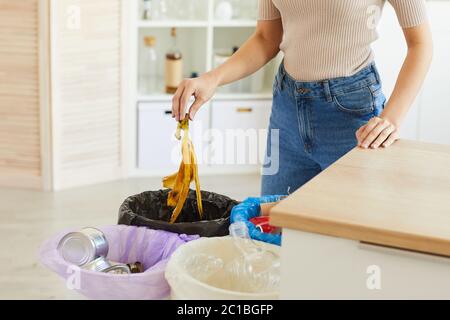 Beschnittene Ansicht einer Frau, die Bananenschale in den Abfalleimer legte. Verschiedene Behälter für die Abfallsortierung in der Küche Stockfoto