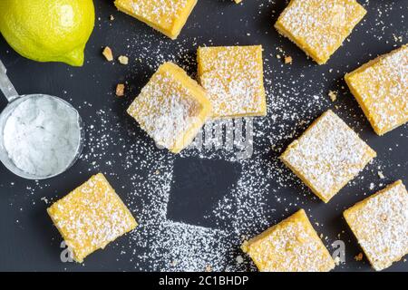 Zitrone Quadrate auf schwarzem Tisch mit Zitrone, Puderzucker - Draufsicht Foto Stockfoto