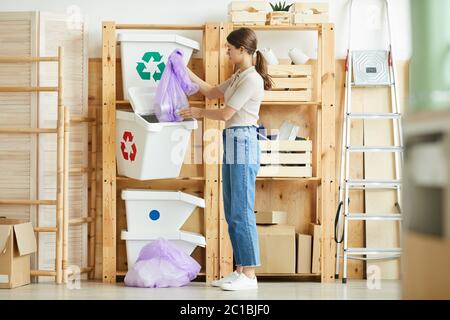 Junge Frau, die das Paket mit Müll in die Plastikbehälter sie den Abfall sortieren Stockfoto
