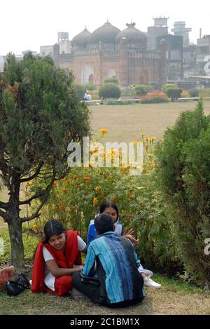Die Einheimischen sitzen und unterhalten sich auf dem Gelände von Lalbagh Fort, Dhaka. Dahinter befindet sich die Moschee des Lalbagh Fort mit drei Kuppeln. Touristenattraktion Dhaka, Bangladesch. Stockfoto