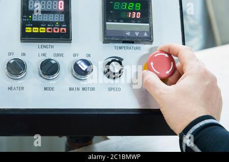 Nahaufnahme der Hand eines Mannes auf einer roten Taste auf dem Bedienfeld. Not-aus oder Start der Anlage und Produktion Stockfoto