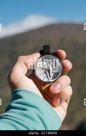 Nahaufnahme DIE Hand EINES Mannes hält einen Taschenkompass vor der Kulisse von Bergen und Wäldern. Das Konzept der Outdoor-Navigation Stockfoto