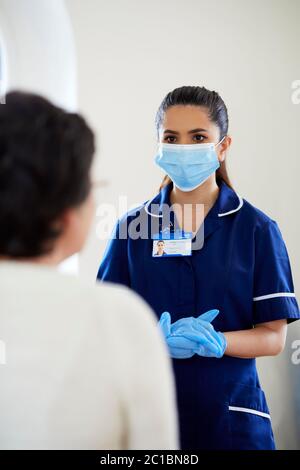 Krankenschwester mit PSA-Maske und Handschuhen, die mit dem Patienten sprechen Stockfoto