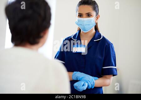 Krankenschwester mit PSA-Maske und Handschuhen, die mit dem Patienten sprechen Stockfoto