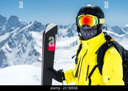 Ein großes Porträt eines Skifahrers in Schutzhelm und Brille - eine Maske und ein Schal neben den Skiern gegen die schneebedeckte mou Stockfoto