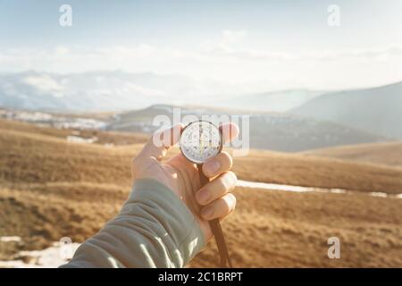 Die Hand eines Mannes hält einen Handkompass vor der Kulisse von Bergen und Hügeln bei Sonnenuntergang. Das Konzept von Reisen und Navigati Stockfoto