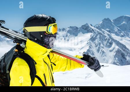 Ein großes Porträt eines Skifahrers in einem Schutzhelm und Brille ist eine Maske und Schal mit Skiern auf der Schulter in der schneebedeckten Stockfoto