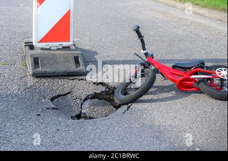 Laufrad (Push Bike) neben Schlagloch auf Asphaltstraße mit Umweg-Warnschild Stockfoto