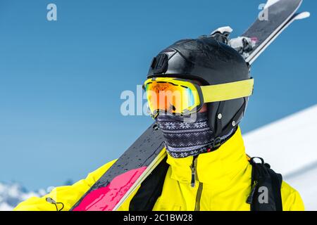 Ein großes Porträt eines Skifahrers in einem Schutzhelm und Brille ist eine Maske und Schal mit Skiern auf der Schulter in der schneebedeckten Stockfoto