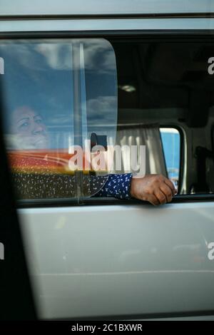 Die Frau, die im Bus sitzt, mit der Hand, die vor dem offenen Fenster hängt und direkt in die Kamera schaut. Stockfoto