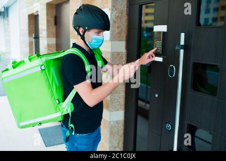 Konzept für die Lebensmittelzustellung. Der Mann, der die Lebensmittel geliefert hat, klingelt an der Sprechanlage Er trägt eine medizinische Maske. Stockfoto
