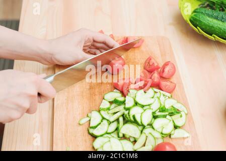 Nahaufnahme zarte weibliche Hände schneiden ein großes Messer mit Tomaten auf einem Viertel auf einem Holzbrett zu Hause. Wohnküche. Gesunde Ernährung Stockfoto