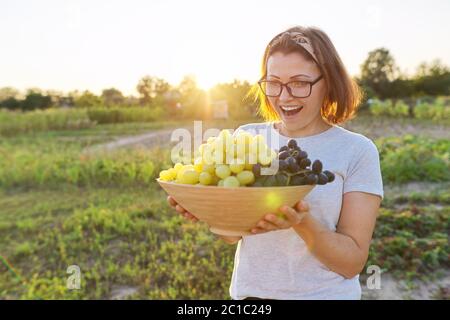 Frau mit Schale frisch gepflückten blauen und grünen Trauben, sonnigen Garten Hintergrund Stockfoto