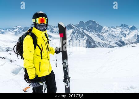 Nahaufnahme eines Skifahrers mit Schutzhelm und Brille. Eine Maske und ein Schal mit einer Eispickel in den Händen neben Skiern Stockfoto