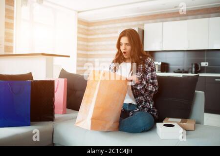 Online einkaufen, bestellte eine junge Frau nach Hause liefern. Jetzt sitzt sie auf der Couch und packt ihre neuen Einkäufe aus Stockfoto