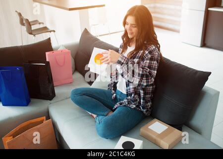 Online einkaufen, bestellte eine junge Frau nach Hause liefern. Jetzt sitzt sie auf der Couch und packt ihre neuen Einkäufe aus Stockfoto