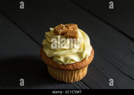 Ein einziger Karamell-Milchbecher Kuchen mit Fudge quadratische Dekoration auf der Oberseite, isoliert auf schwarzem Holz BA Stockfoto