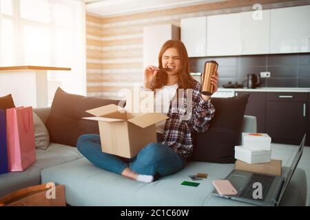 Online einkaufen, bestellte eine junge Frau nach Hause liefern. Jetzt sitzt sie auf der Couch und packt ihre neuen Einkäufe aus Stockfoto