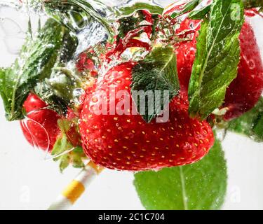Nahaufnahme der kalten und frischen Limonade mit Erdbeere, Minzblättern und Eiswürfeln. Textur des kühlenden Sommergetränks mit Makroblasen auf Glas. Auf der Oberfläche schwimmend oder schwimmend. Stockfoto