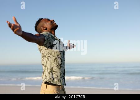 Ein afroamerikanischer Mann mit ausgestreckten Armen am Strand an einem sonnigen Tag Stockfoto