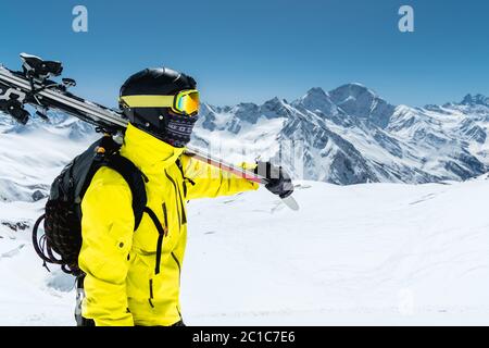 Ein großes Porträt eines Skifahrers in einem Schutzhelm und Brille ist eine Maske und Schal mit Skiern auf der Schulter in der schneebedeckten Stockfoto