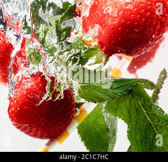 Nahaufnahme der kalten und frischen Limonade mit Erdbeere, Minzblättern und Eiswürfeln. Textur des kühlenden Sommergetränks mit Makroblasen auf Glas. Auf der Oberfläche schwimmend oder schwimmend. Stockfoto