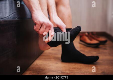 Nahaufnahme. Ein Mann legt eine Socke auf den Hintergrund der Schuhe. Er sitzt auf seinem Bett. Stockfoto