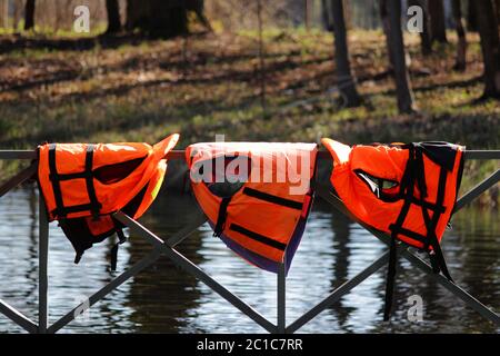 Drei orangefarbene Rettungswesten hängen an der Reling nahe dem Pier an der Bootstation. Gattschina, Russland. Stockfoto