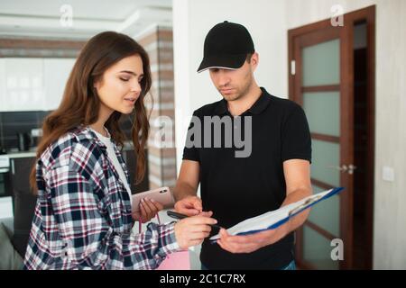 Lieferung von Waren und Einkäufe nach Hause. Der Kurier oder Liefermann übergibt das Paket mit der Ware an eine junge Frau. Sie unterschreibt die Dokumente für t Stockfoto