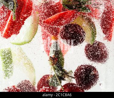 Nahaufnahme von kalten und frischen Limonaden mit Erdbeere, Kirsche, Minzblättern und Eiswürfeln. Textur des kühlenden Sommergetränks mit Makroblasen auf Glas. Auf der Oberfläche schwimmend oder schwimmend. Stockfoto