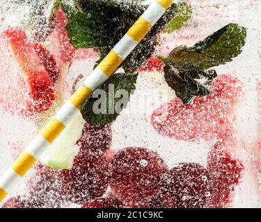 Nahaufnahme von kalten und frischen Limonaden mit Erdbeere, Kirsche, Minzblättern und Eiswürfeln. Textur des kühlenden Sommergetränks mit Makroblasen auf Glas. Auf der Oberfläche schwimmend oder schwimmend. Stockfoto