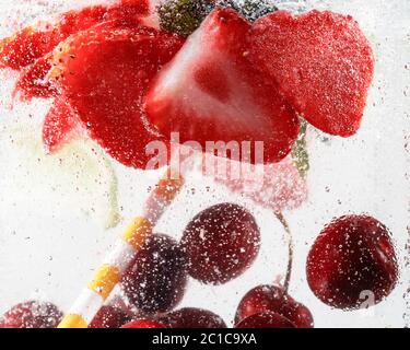 Nahaufnahme von kalten und frischen Limonaden mit Erdbeere, Kirsche, Minzblättern und Eiswürfeln. Textur des kühlenden Sommergetränks mit Makroblasen auf Glas. Auf der Oberfläche schwimmend oder schwimmend. Stockfoto