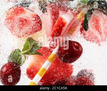 Nahaufnahme von kalten und frischen Limonaden mit Erdbeere, Kirsche, Minzblättern und Eiswürfeln. Textur des kühlenden Sommergetränks mit Makroblasen auf Glas. Auf der Oberfläche schwimmend oder schwimmend. Stockfoto