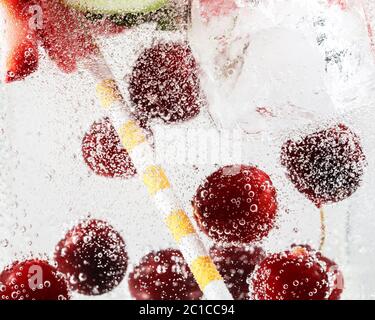 Nahaufnahme von kalten und frischen Limonaden mit Erdbeere, Kirsche, Minzblättern und Eiswürfeln. Textur des kühlenden Sommergetränks mit Makroblasen auf Glas. Auf der Oberfläche schwimmend oder schwimmend. Stockfoto