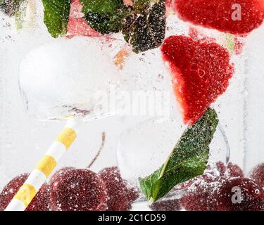 Nahaufnahme von kalten und frischen Limonaden mit Erdbeere, Kirsche, Minzblättern und Eiswürfeln. Textur des kühlenden Sommergetränks mit Makroblasen auf Glas. Auf der Oberfläche schwimmend oder schwimmend. Stockfoto